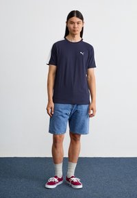 Marineblå crew-neck t-shirt med hvide ærmer, parret med lyseblå denim shorts. Bærer bordeaux sneakers og grå sokker. Simpelt design, sporty look.