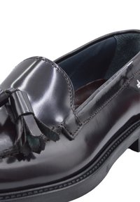 Zwarte gepatineerde leren instapper met een kwastaccent, gladde oppervlakken, ronde neus, gestikte details en een dikke zwarte rubberen zool.