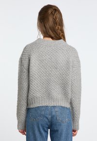 Pulover gri tricotat, cu un model texturat, de lungime scurtă și cu margine ribotată. Asortat cu blugi din denim albastru, cu talie înaltă.