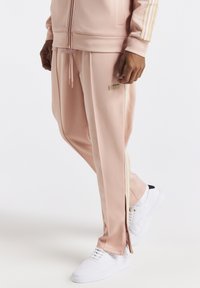 Růžové teplákové kalhoty z hladké látky, s zlatými bočními pruhy, zipy u kotníků a malou logo nášivkou.