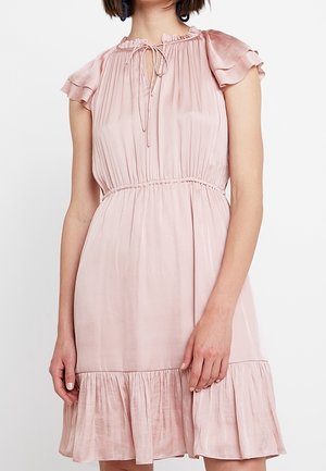 Mujer que lleva un vestido rosa claro, de manga corta, hasta la rodilla, con un dobladillo con volantes, cintura ceñida y detalle de lazo en el escote.