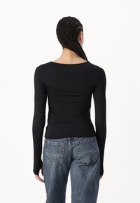 Black long-sleeve top with a snug fit, featuring a round neckline and gathered detailing at the back, paired with blue high-waisted jeans.