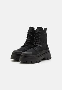 Botines negros con cordones, que cuentan con un empeine de textil, suela de goma, plataforma gruesa, punta redondeada y acentos de metal.