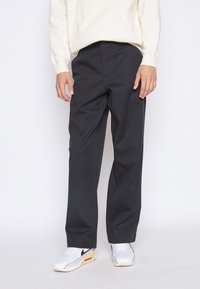 Mustat housut rentoa mallia, joissa on sileä pinta, tasainen etuosa ja sivutaskut. Yhdistetty vaaleanbeigeen huppariin ja valkoisiin lenkkareihin.