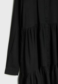 Svart knapp-up klänning med tierad design, mjukt tyg, långa ärmar och lätt rynkning vid Midjan för volym.