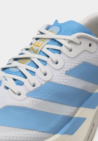 Baskets blanches et bleu clair avec des lacets blancs, des panneaux texturés et un texte jaune sur la partie de la languette bleue.