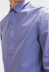 Jasnofioletowa koszula na guziki z teksturowanym wzorem, kołnierzykiem z ciemną lamówką i klasycznymi mankietami.