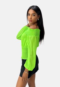 Jasnozielony top odkrywający ramiona z marszczonym wzorem na klatce piersiowej i rękawach, zestawiony z czarną spódnicą. Gładka tkanina, rozkloszowane rękawy.