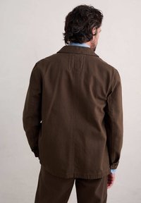 Brązowa kurtka z fakturowanej tkaniny, z karczkiem z tyłu, długimi rękawami i mankietami zapinanymi na guziki, w zestawie z dopasowanymi spodniami.