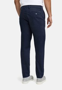Pantaloni chinos blu navy in misto cotone, con taglio dritto, tasca posteriore con bottone e tessuto liscio. Abbinati a sneakers grigie.
