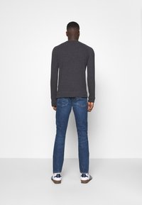 Mörkgrå långärmad tröja i kombination med blå jeans och vita sneakers med blå ränder, sedd bakifrån.