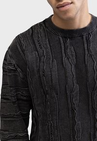 Black textured sweater with vertical ribbed patterns, round neck, and knitted trim. Material appears soft with varying fabric thickness.