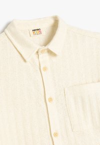 Lichtcrème button-down shirt met een gestructureerd ruitpatroon, voorzien van een kraag, een borstzak en gele knopen.
