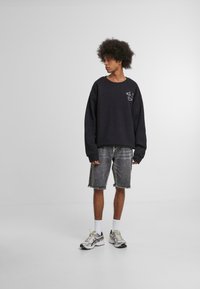 Sweatshirt noir oversize avec détail de logo, associé à un short en denim gris avec ourlets effilochés, et des chaussettes blanches avec des baskets grises.