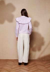 Λευκό παντελόνι με φαρδιές φάσες συνδυασμένο με ροζ και λευκό ριγέ μπλουζάκι με βολάν στο γιακά, απεικονιζόμενο από πίσω σε υφή φόντου.