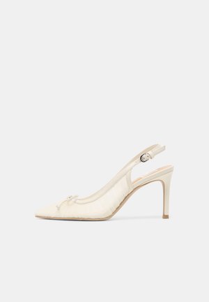 Kremowy sandał na wysokim obcasie z odkrytą piętą, spiczastym noskiem, małą kokardką i regulowanym paskiem z klamrą na jednolitym tle.