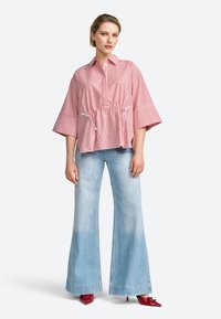 Camicia over size a righe rosse e bianche con vita cintrata, maniche corte, abbinata a jeans a gamba larga azzurri e scarpe con tacco rosse.