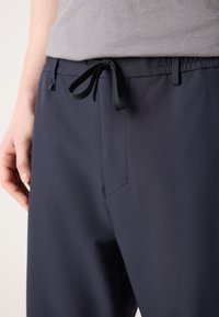 Marineblauwe elastische taillebroek met een zwarte trekkoord, voorzien van een zijzak en een gladde stoftextuur.