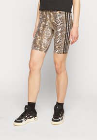 Bruna och vita cykelshorts med ormskinsmönster, svarta sidoränder och en Adidas-logotyp. Figurnära design gjord av stretchigt material.