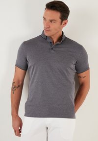 Grå kortärmad polo med krage och tre knappar, med kontrasterande mörka detaljer på ärmarna och en figursydd design.