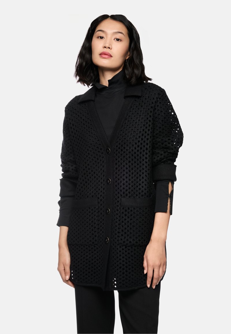 Schwarze Strickjacke mit einem Wabenmuster, zwei frontalen Taschen und Knöpfen. Das Design umfasst einen Kragen und gerippte Ärmelbündchen.