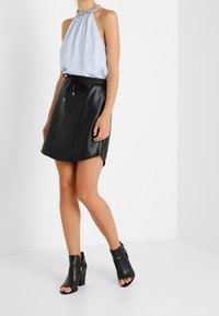 Ljusblå halterneck-topp med en pärlkrage, i kombination med en svart mini kjol i konstläder och svarta peep-toe högklackade stövlar.