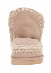 Lyserød ruskinds-slippers med dekorativt flettet trim, rund form, tykk sål og subtile syningsdetaljer langs kanterne.