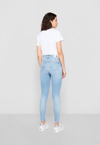Jasnoniebieskie skinny jeans z denimu o wysokim stanem i tylnymi kieszeniami, zestawione z białą koszulką z krótkim rękawem i białymi sneakersami.