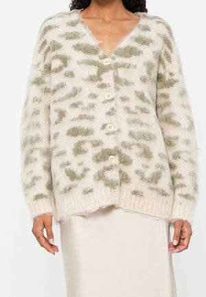 Cardigan duveteux blanc et gris à boutons avec un motif abstrait porté sur une jupe claire sur une personne.