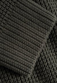 Mörkgrått stickat tyg med ribb- och våffelmönster, som visar tjocka fibrer och en mjuk, något lös väv.