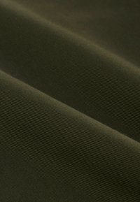 Ciemnozielony żebrowany materiał złożony wzdłuż przekątnej, ukazujący teksturę i drobne poziome linie.