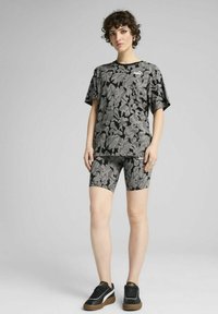 Camisa de manga corta negra y gris con un patrón gráfico y pantalones cortos de ciclismo a juego, hechos de un material suave, complementados con zapatillas negras con suelas de goma.