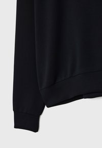 Sweatshirt noir avec une texture lisse, des manches longues et des poignets côtelés, à coupe décontractée sans motifs ni accessoires visibles.