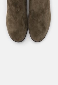 Olivgrüne Wildleder-Stiefeletten mit glatter Textur, abgerundeter Spitze und flacher Sohle, von oben betrachtet, um die Form und das Design zu betonen.