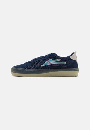 Zapatillas de color azul marino hechas de malla y ante, con una parte superior texturizada, suela de goma y un distintivo detalle de raya azul en el costado.