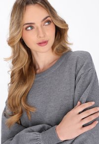 Grauer Pullover mit Rundhalsausschnitt, weicher Textur und lockeren Ärmeln. Der Stoff wirkt leicht und gemütlich.