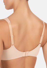 Beige rintaliivi, jossa on säädettävät hihnat, sileä materiaali ja hakaskiinnitys selässä. Saumaton muotoilu ilman näkyviä kuvioita.