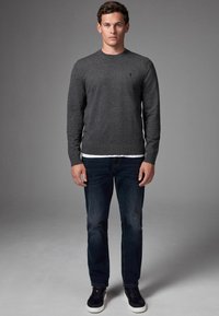 Grå stickad tröja med rund halsringning, matchad med mörka jeans och svarta sneakers med vita sulor. En enkel och klassisk design.