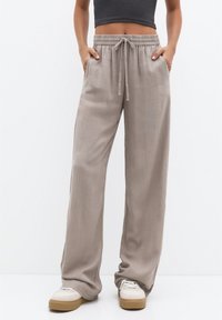 Světle béžové kalhoty s širokými nohavicemi vyrobené z měkké texturované tkaniny. Mají elastický pas se stahovací šňůrkou a boční kapsy.