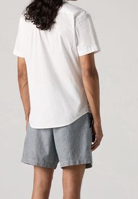 Weißes kurzärmeliges Hemd mit geschwungenem Saum, kombiniert mit grau-weiß gestreiften Shorts. Die Shorts verfügen über Seitentaschen und einen lockeren Schnitt.