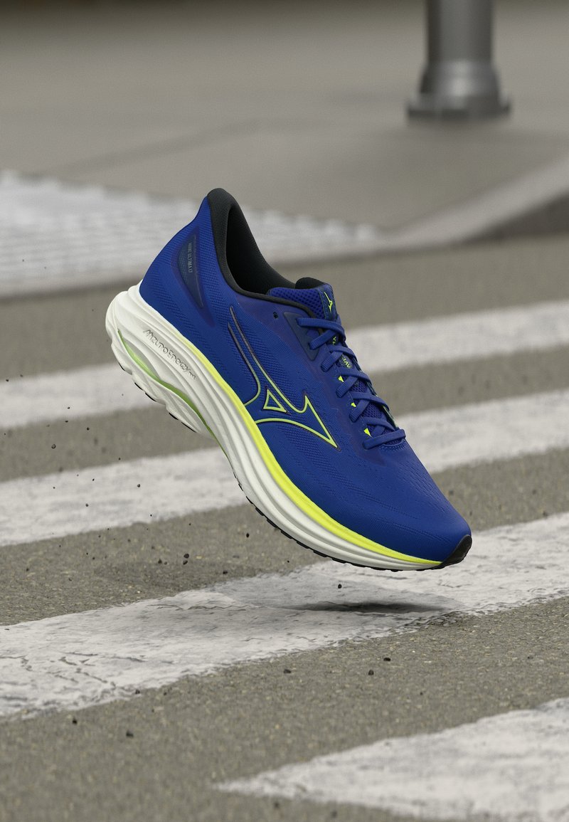 Μπλε αθλητικό παπούτσι με λευκή και κίτρινη σόλα να αιωρείται πάνω από μια διάβαση πεζών σε πλακόστρωτο δρόμο.