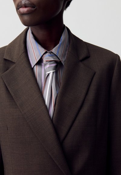 Blazer marrone su misura con rever eleganti, abbinato a una cravatta e a una camicia a righe grigie e pastello. Tessuto liscio, taglio moderno.