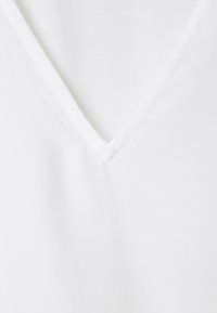 Hvid V-hals top lavet af blødt stof. Har en glat tekstur med et rent, enkelt design. Ingen mønstre eller bemærkelsesværdige metaldele.