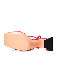 Punaiset korkokengät, joissa on ohuet nauhat, neliömäinen etuosa ja teksturoitu musta kolmio-osa. Sujuva beige pohja, jossa on hienovarainen brändäysdetails.