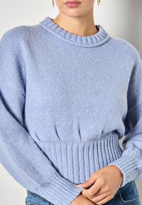 Jasnoniebieski sweter robiony na drutach z ribbowym pasem i mankietami, okrągłym dekoltem i miękką fakturą. Posiada luźny krój z bufkami na rękawach.