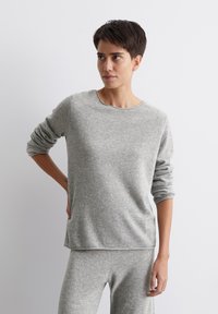 Szary sweter z długim rękawem, wykonany z miękkiego dzianiny, z okrągłym dekoltem i podwiniętymi rękawami, w zestawie ze spodniami w tym samym odcieniu. Gładka tekstura.