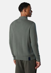 Maglione lavorato a maglia verde chiaro con colletto ripiegato, caratterizzato da un bordo a costine e un accento blu navy sul retro. Tessuto liscio e texturizzato.