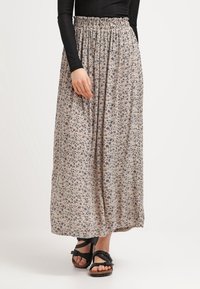Maxi-rok met elastische tailleband, gemaakt van lichtgewicht stof. Kenmerkt een bloemenprint in gedempte kleuren. Gestyled met zwarte sandalen.