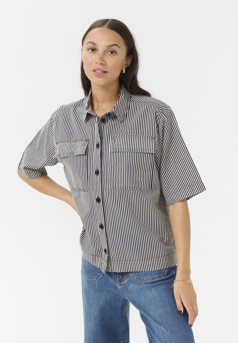 Chemise à rayures bleu et blanche en coton, dotée de deux poches poitrine et d'une fermeture à boutons noirs sur le devant.