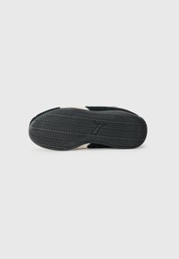 Semelle de chaussure de sport noire avec profils en caoutchouc texturé, dotée d'un intercalaires blanc. Le design est épuré et minimal, mettant en avant la traction et la durabilité.